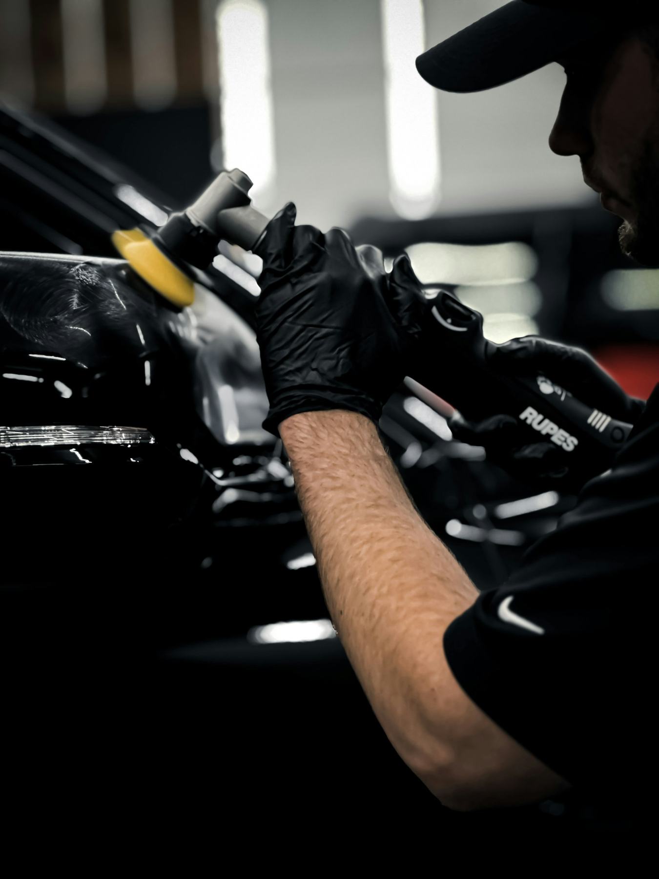A detailer machine-polishing the hood of a black car